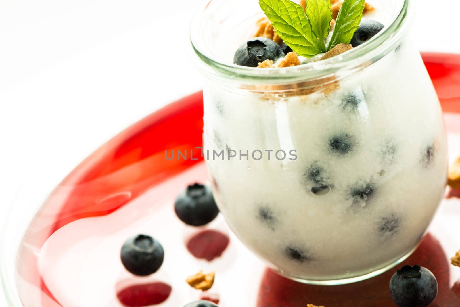 Glass of yoghurt with berries and mint on a plate