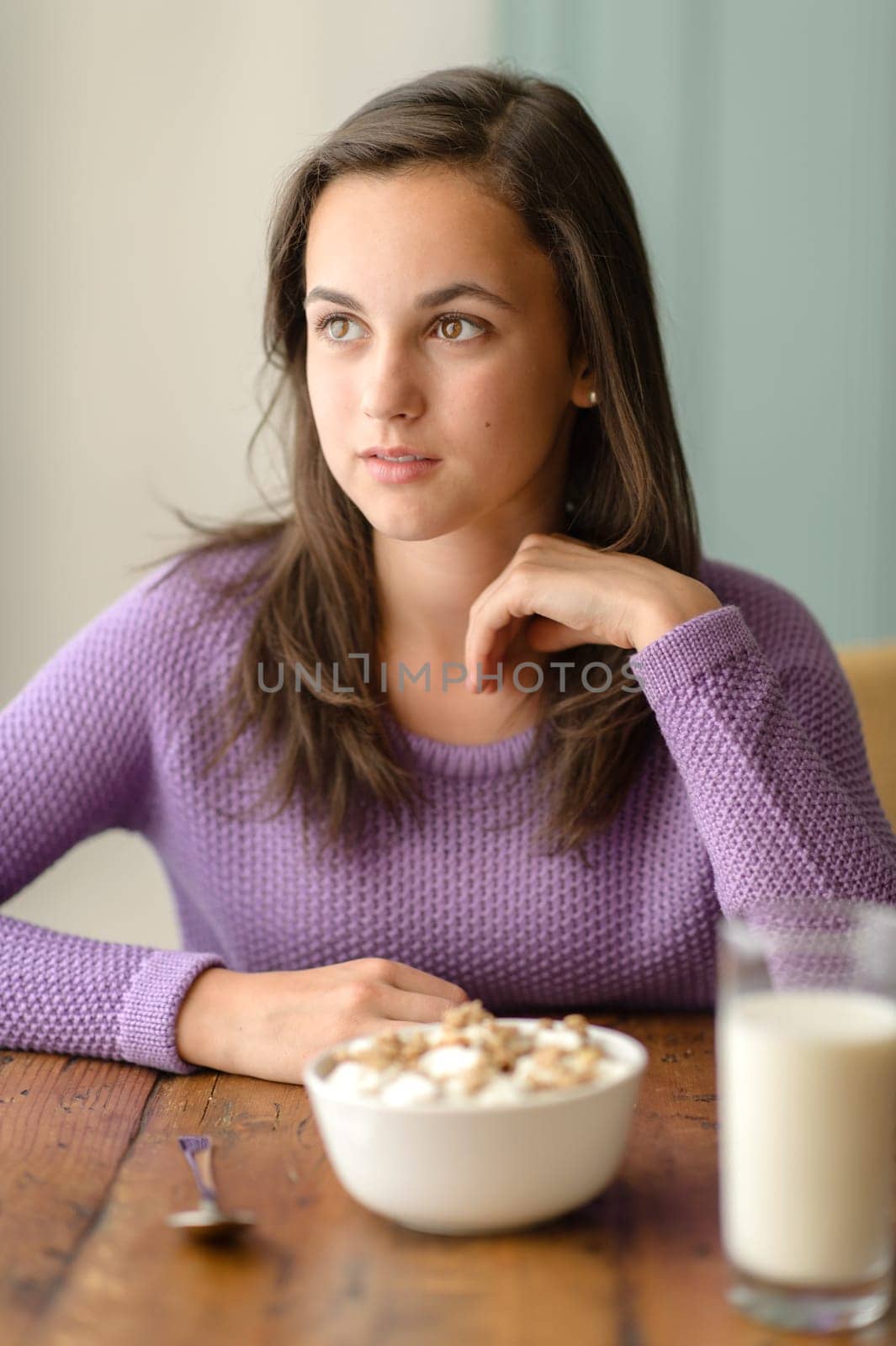 Thoughtful young woman with cereal breakfast wooden table looking aside