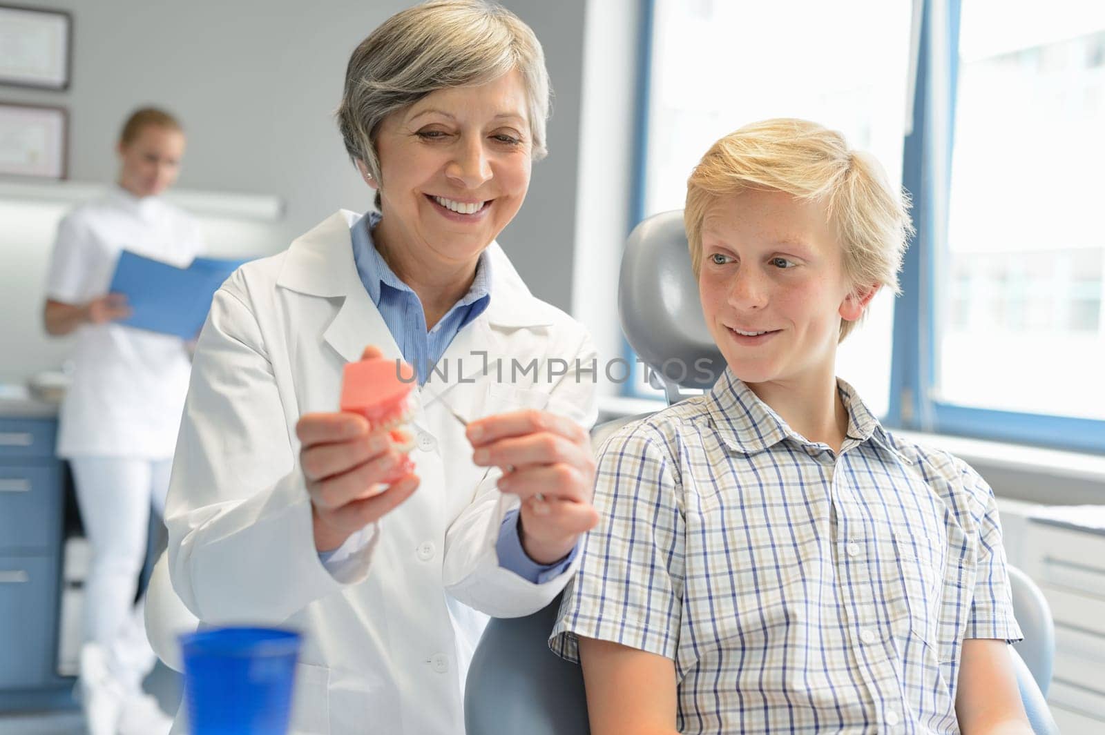 Dentist show teenage patient teeth dentures assistant at dental clinic