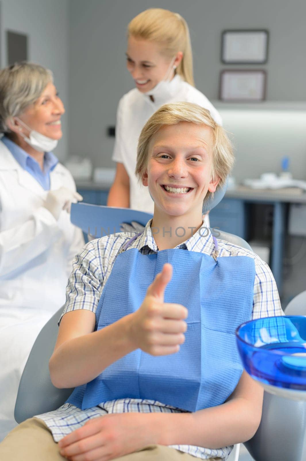 Teenager patient thumbup at dental surgery dentist and nurse background