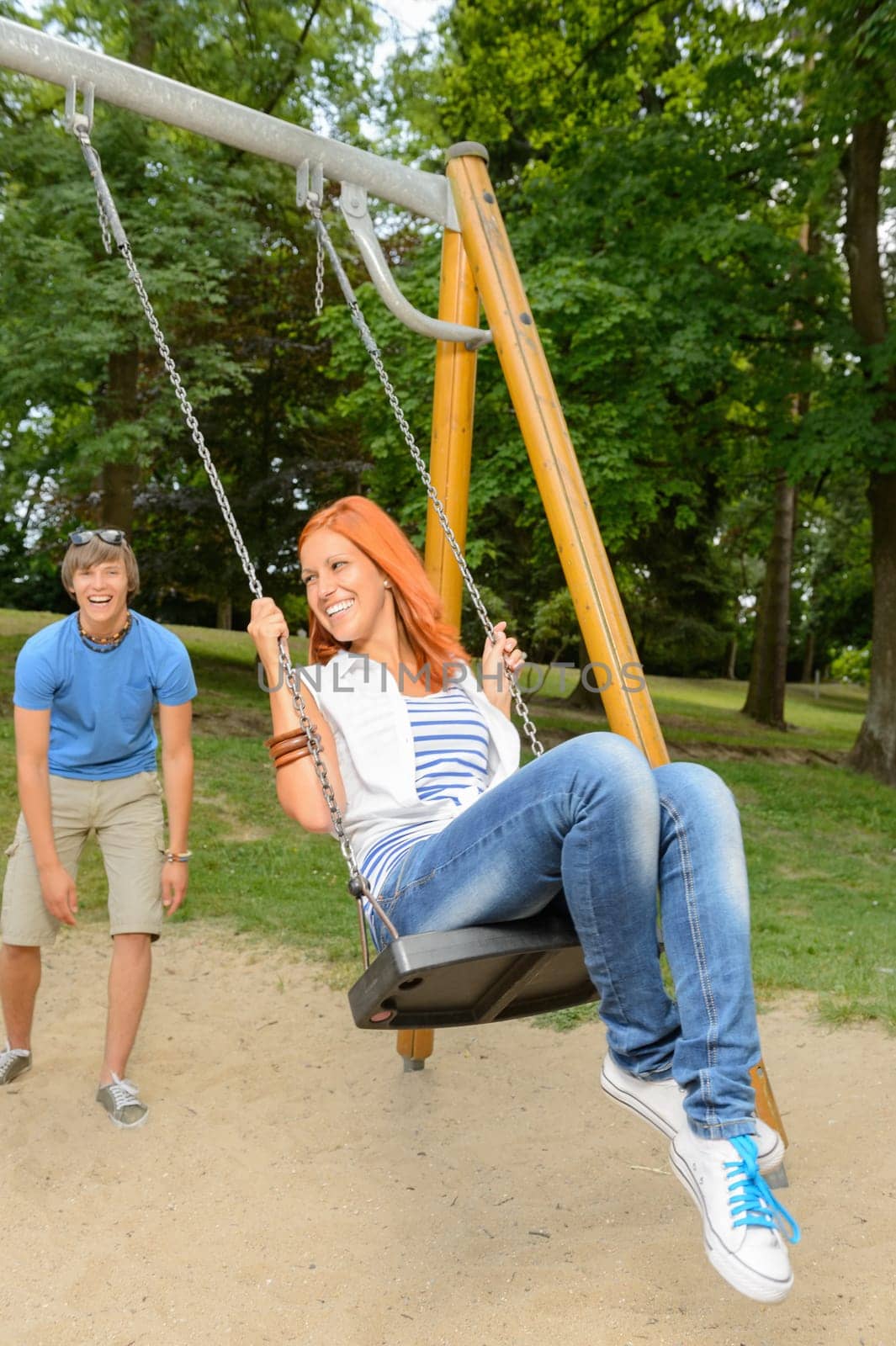 Playful teenage couple girl sitting on swing in park