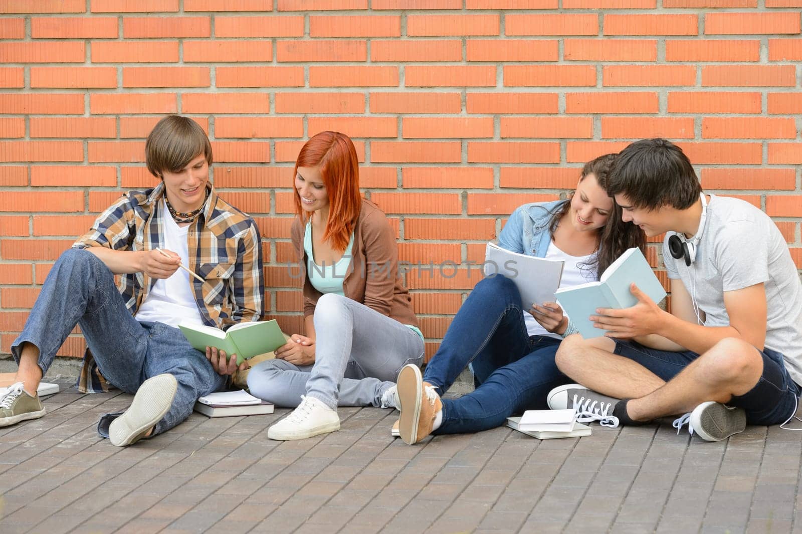 Group of students with books hanging out sitting against wall