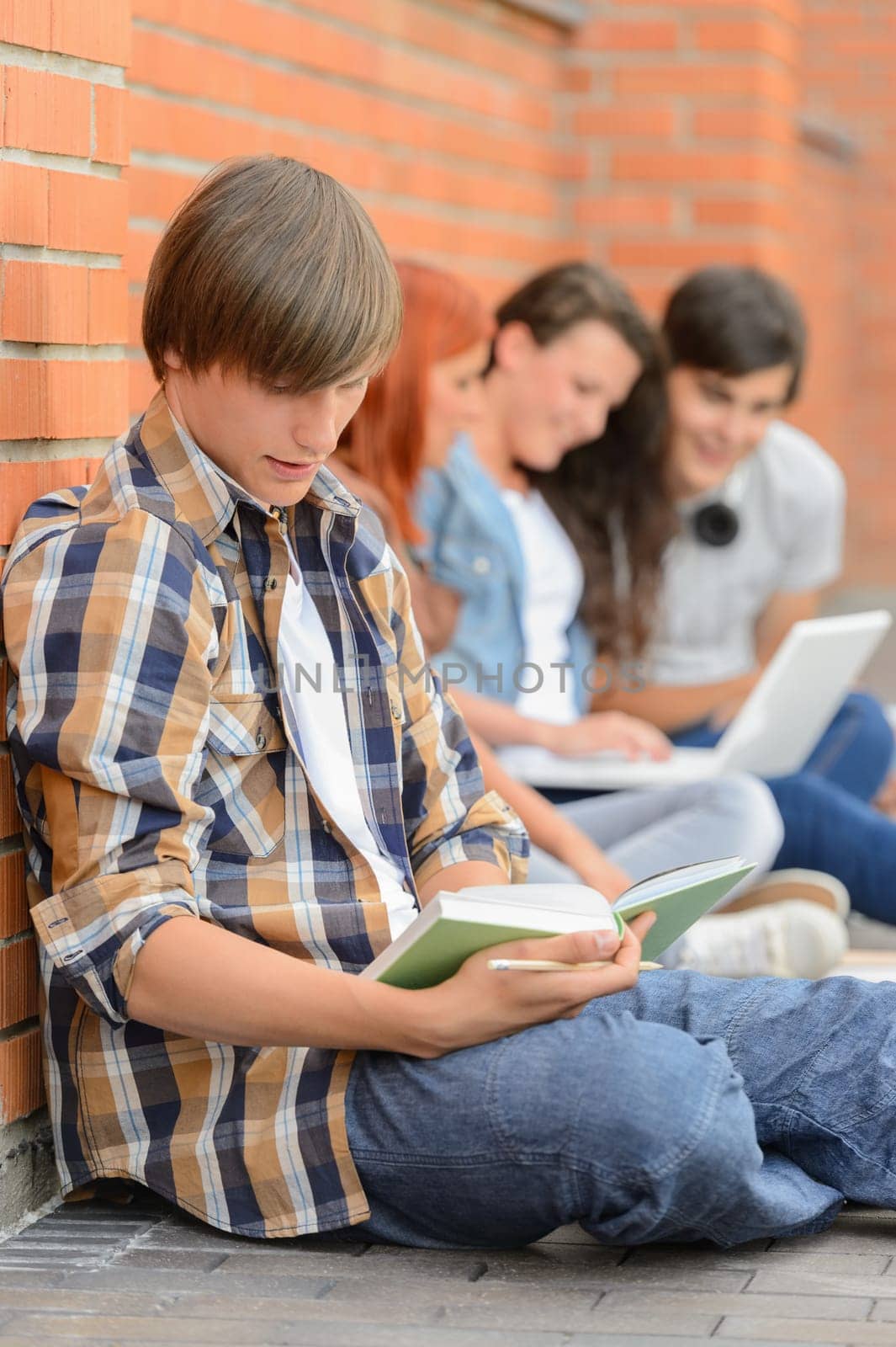 Young man studying book college friends sitting ground using laptop