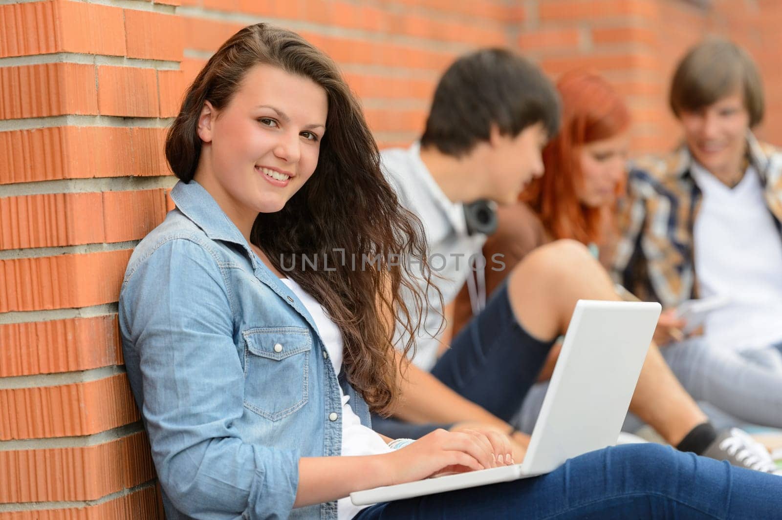 Student girl sitting with laptop outside campus friends in background