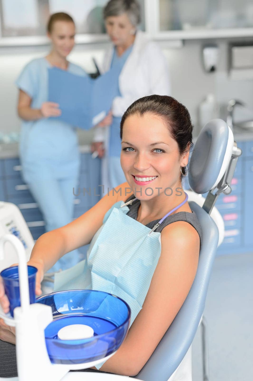Woman patient sitting chair dental surgery checkup professional dentist team background