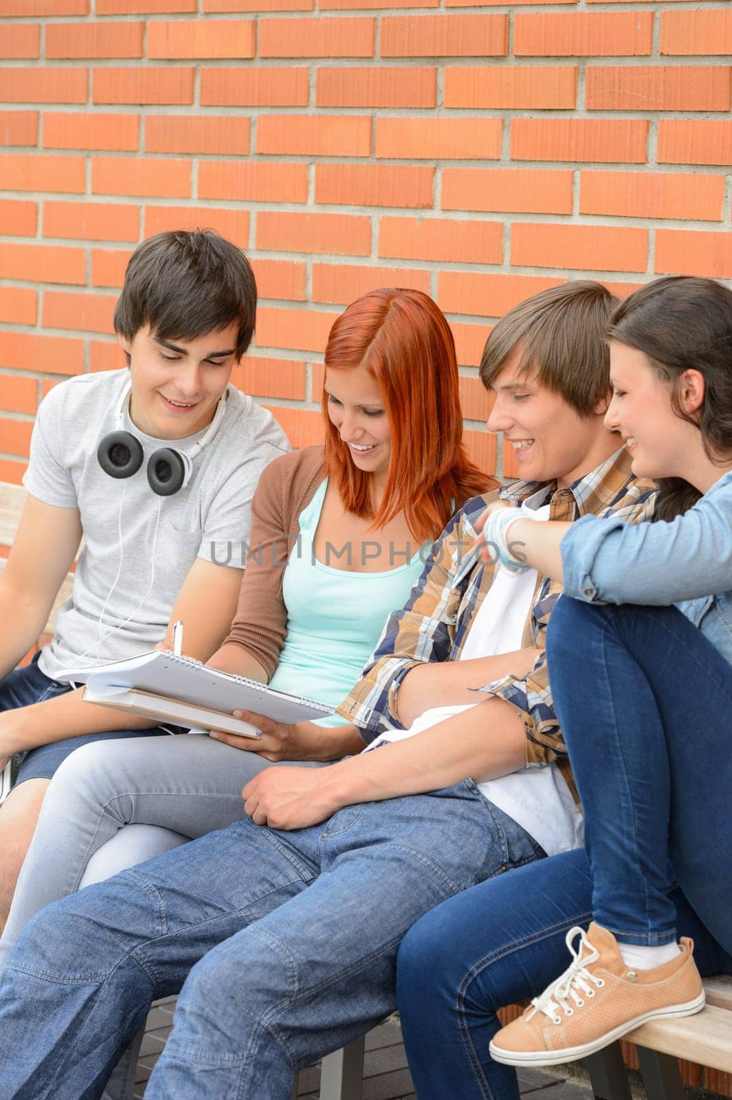 Group of students sitting bench outside college writing notes brainstorming