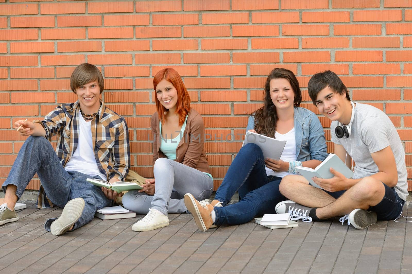 College students with books sitting ground by brick wall