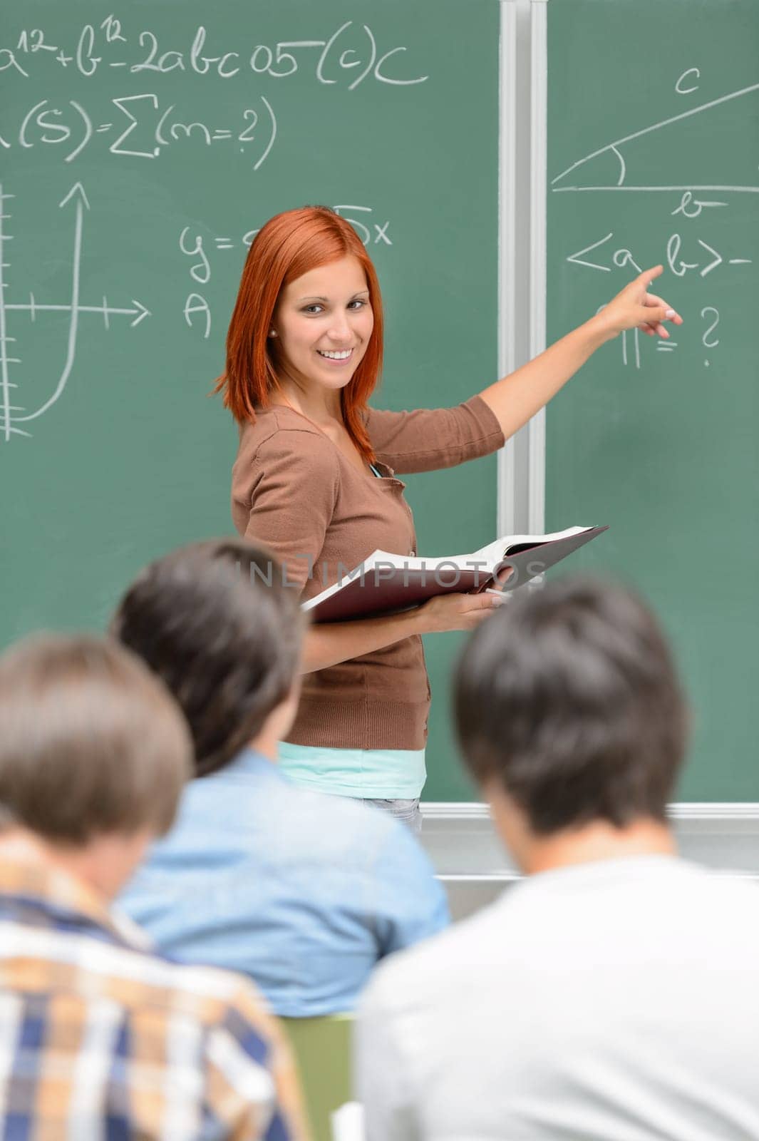 Mathematics student girl pointing on chalkboard looking at classmates