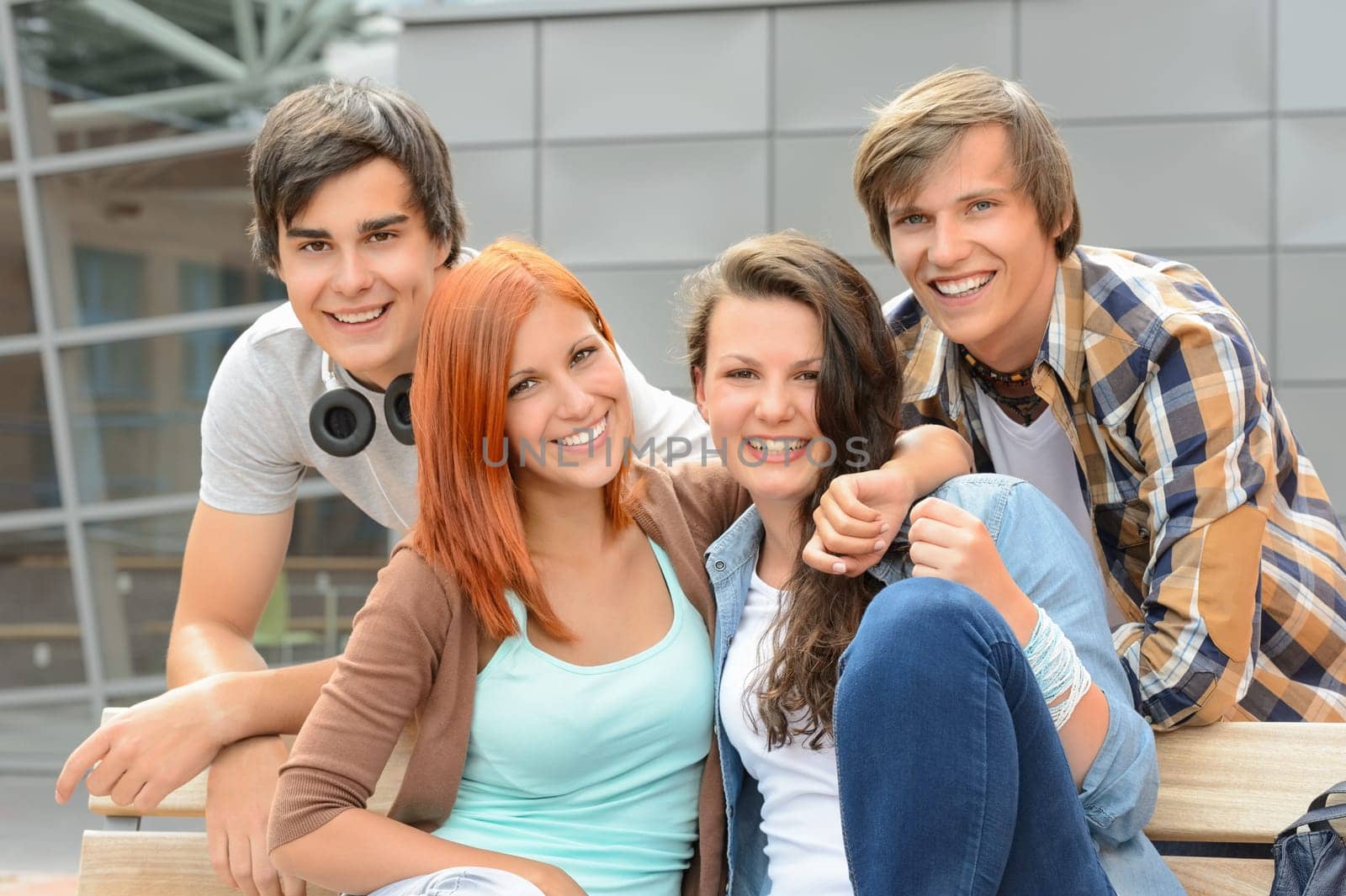 Cheerful group of student friends hugging together outside college