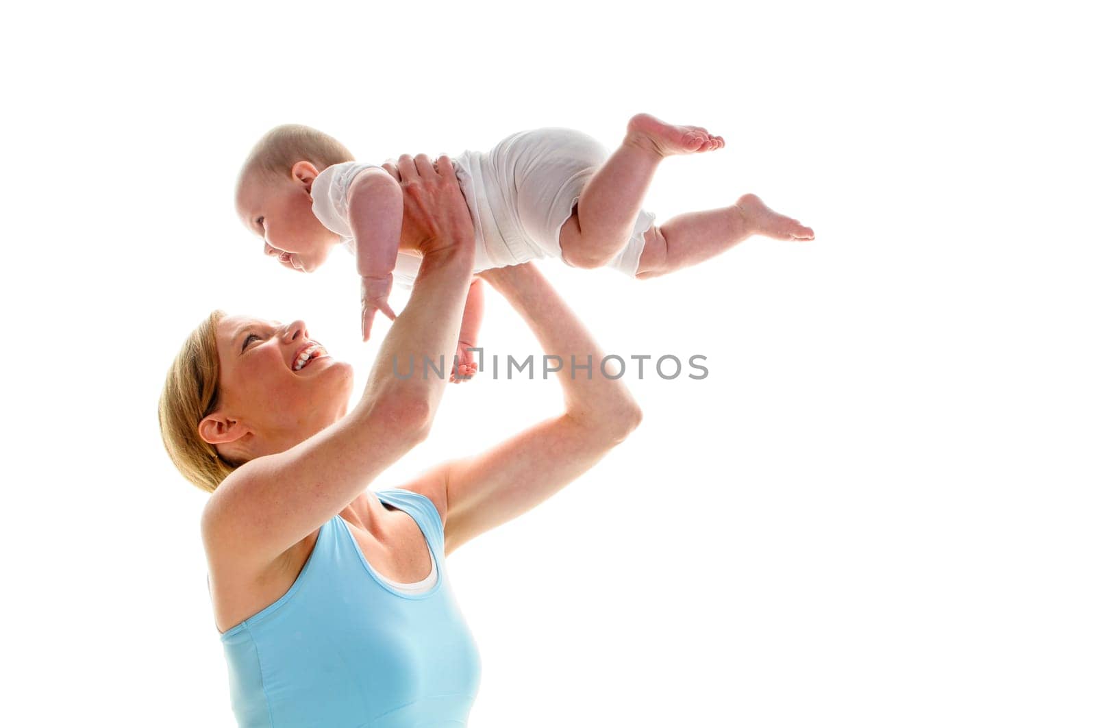 Young mother does back-education gymnastics with her 6-month-old daughter,isolated against a white background. She kneels on the ground and lifts the baby up and laughs.