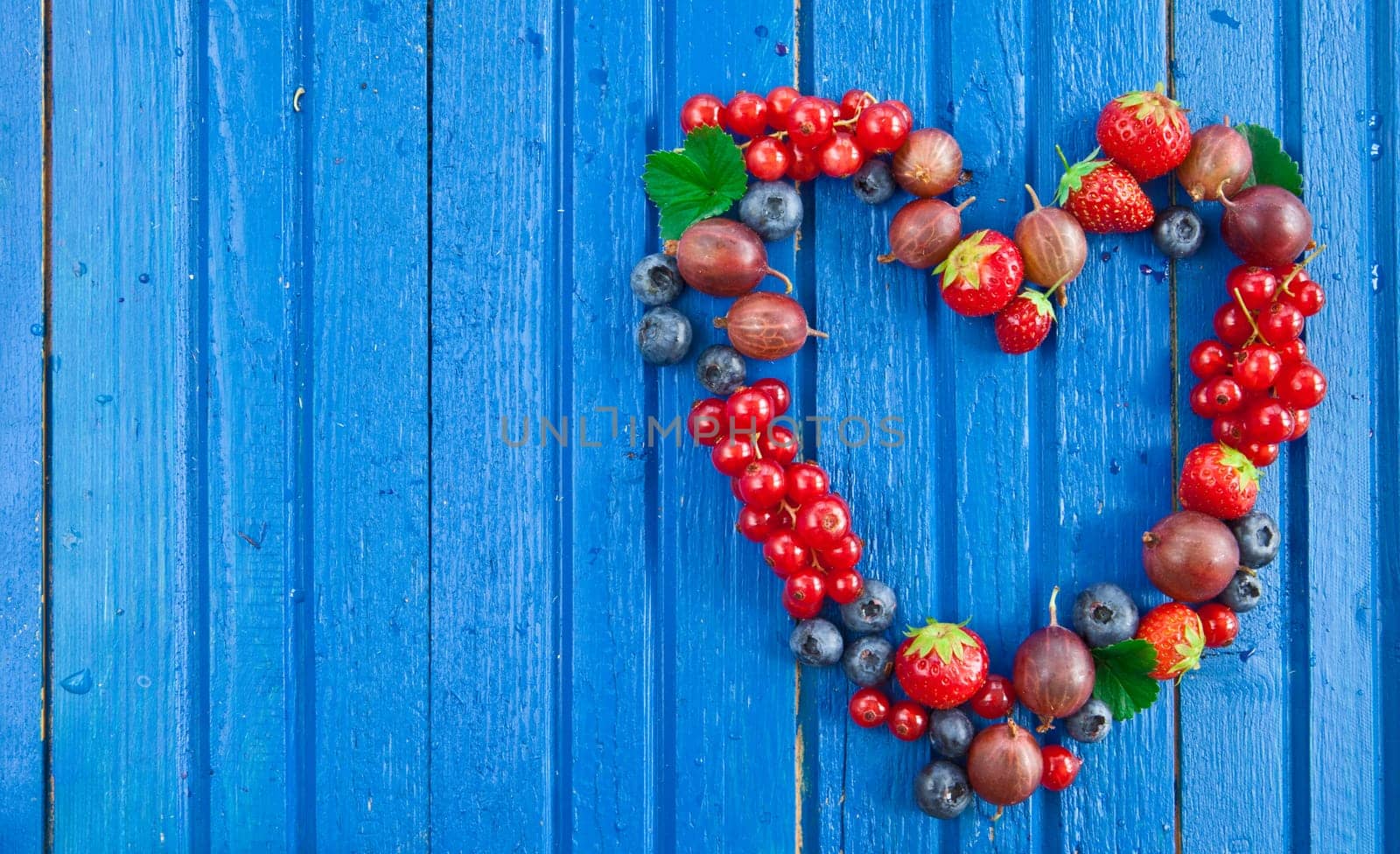 Blue background with fresh summer berries in heart shape