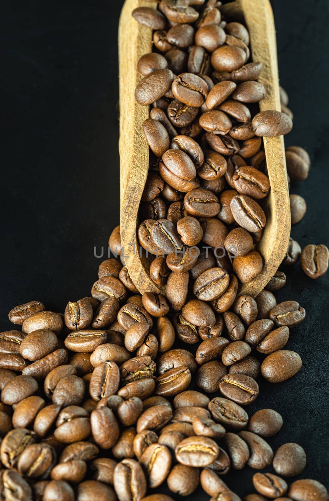 View of Roasted coffee beans on a rich textured surface in Wooden coffee scoop on Black background. Enjoy your morning coffee for living, use it as your Copy space, Design, Wallpaper and Poster, Selective focus.