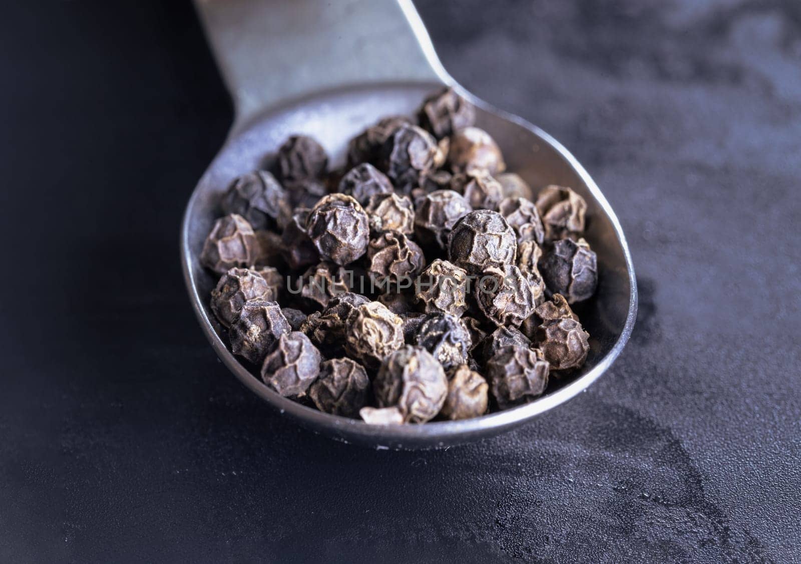 Raw organic black peppercorns or Dry black pepper seeds in stainless steel spoon on Dark background. use it as your Copy space, Design, Wallpaper and Poster, Selective focus.