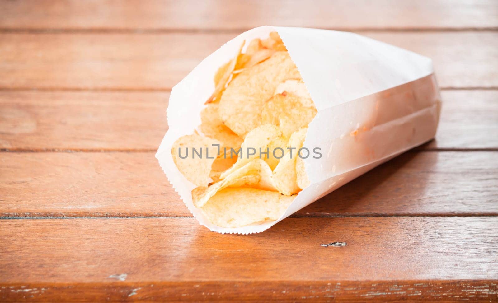 Potato chips in paper bag on wood table