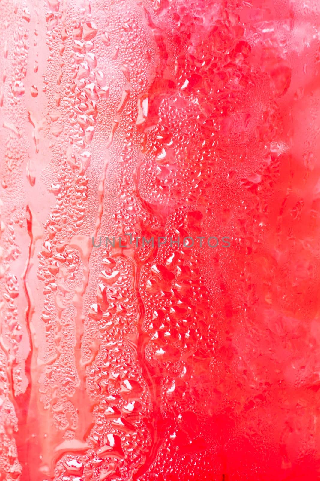Glass surface of red drink with ice cubes background