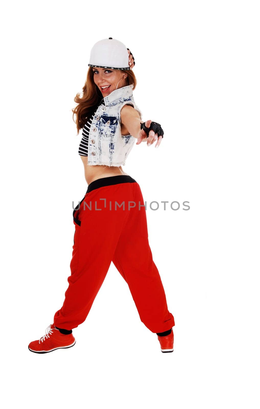 A lovely woman in red pants, jeans jacket and a hat standing in profile and.pointing with her finger, isolated on white background..