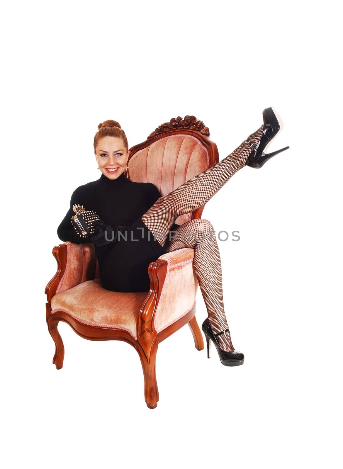 A pretty woman in a black dress sitting in a pink armchair lifting one leg .up into the air, isolated for white background..