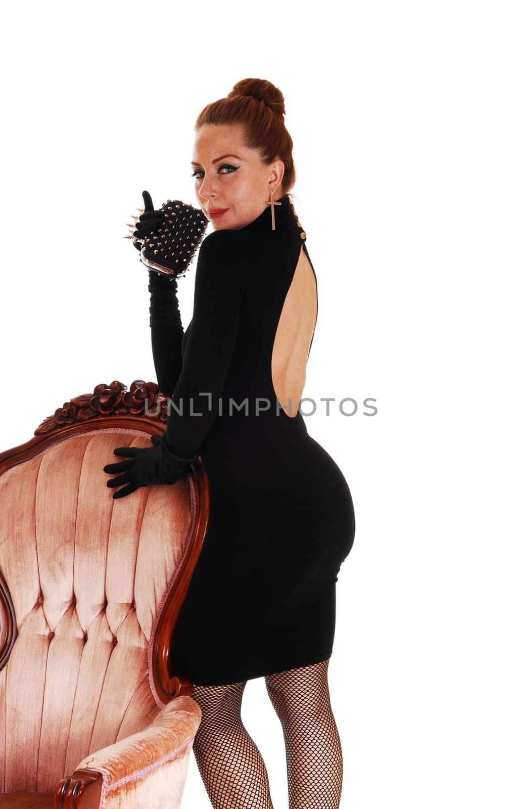 A lovely slim woman in a black dress standing on a pink.armchair, isolated for white background..