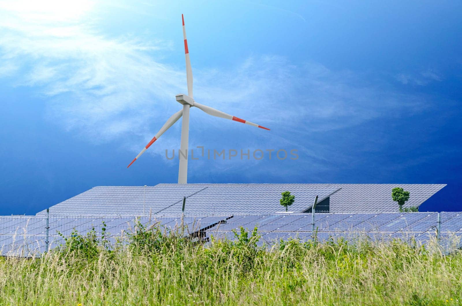 Solar cells and wind turbine on the green meadow in front of blue sky with sun rays