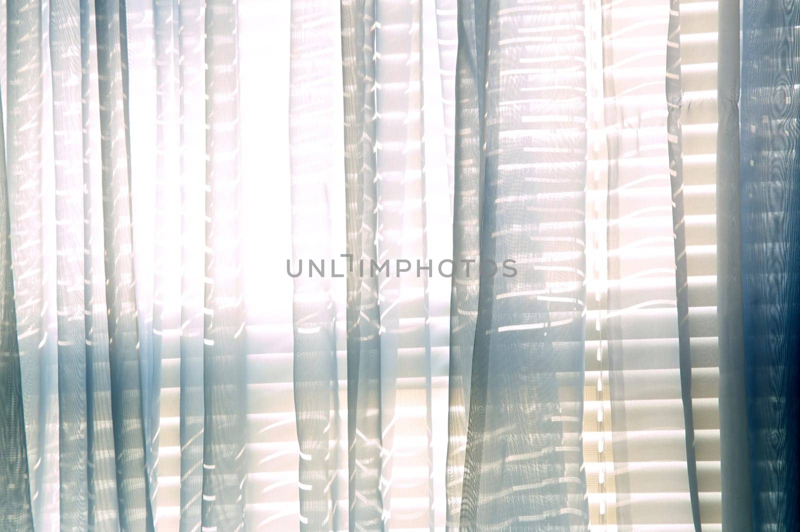 Bright daylight shines through a window draped with blue sheer curtains in this semi abstract high key image.
