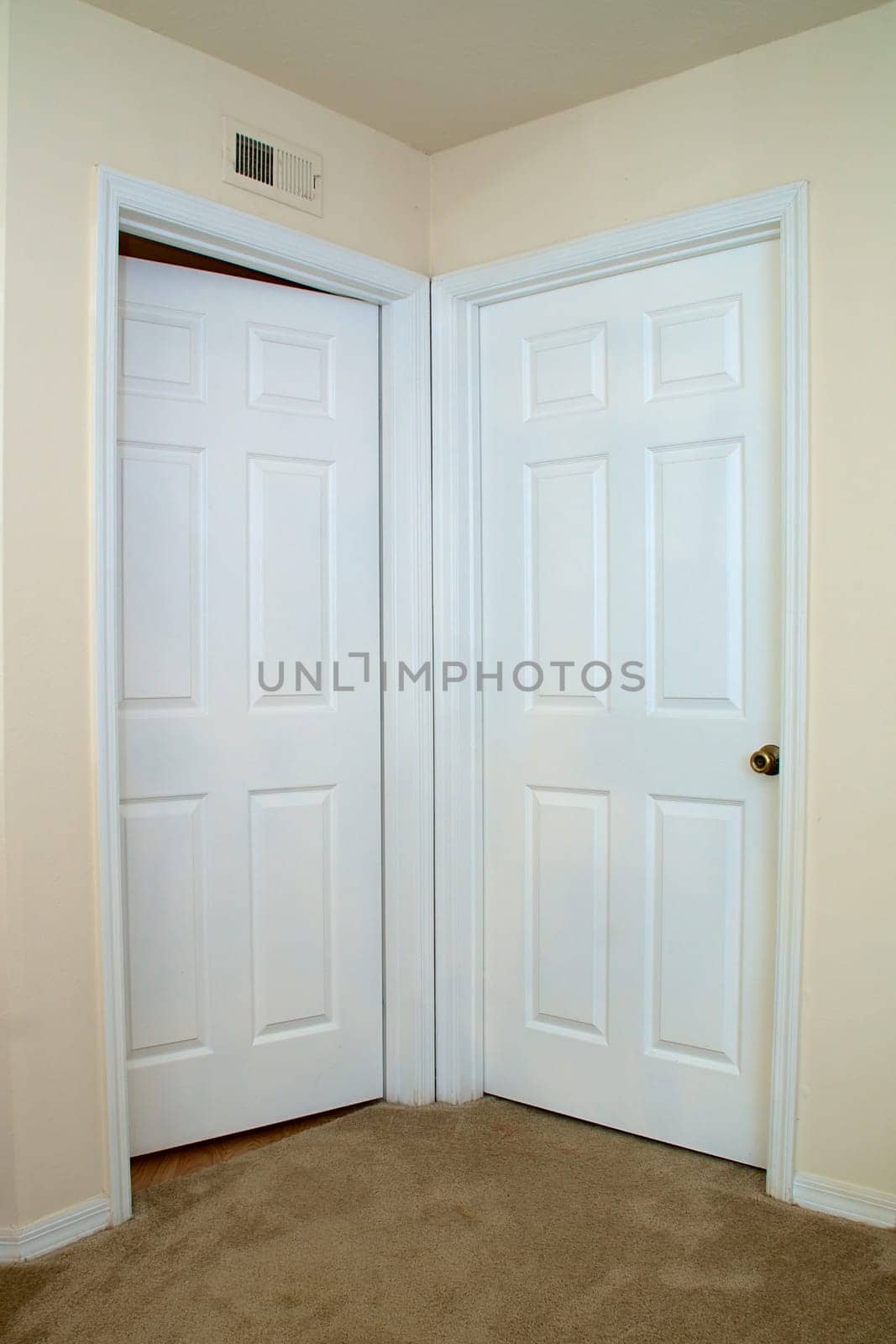 View of two white interior doors one closed, the other is ajar or slightly open in carpeted room.