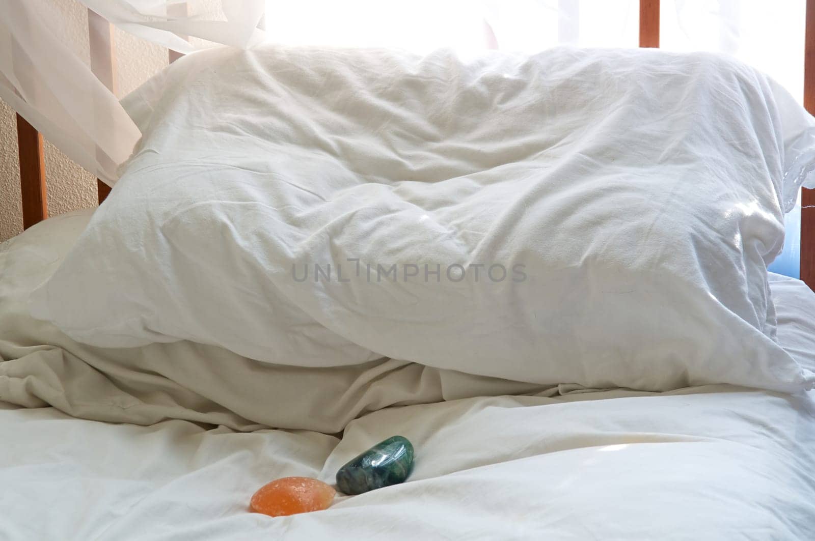 Shot under natural light, two healing stones are close to pillows on a bed.