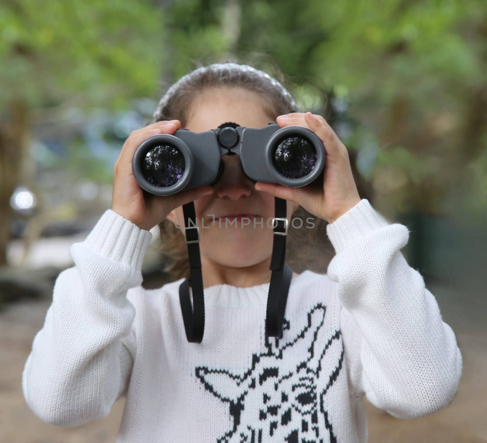 Little girl in white jumper looking through binoculars