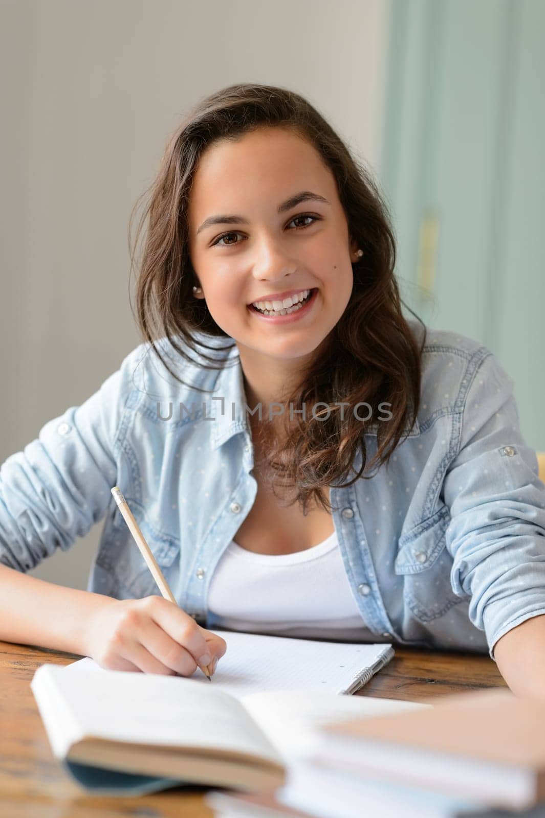 Teenage student girl studying at home smiling at camera