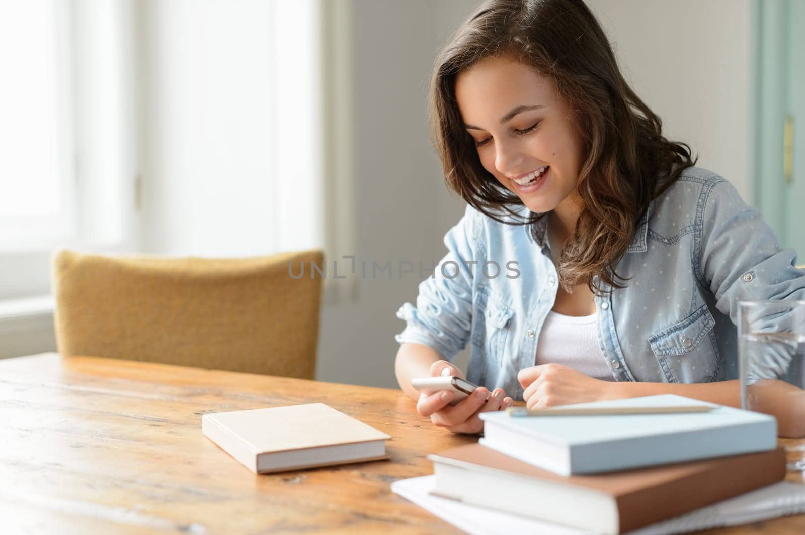 Teenage girl at home looking mobile phone smiling studying books