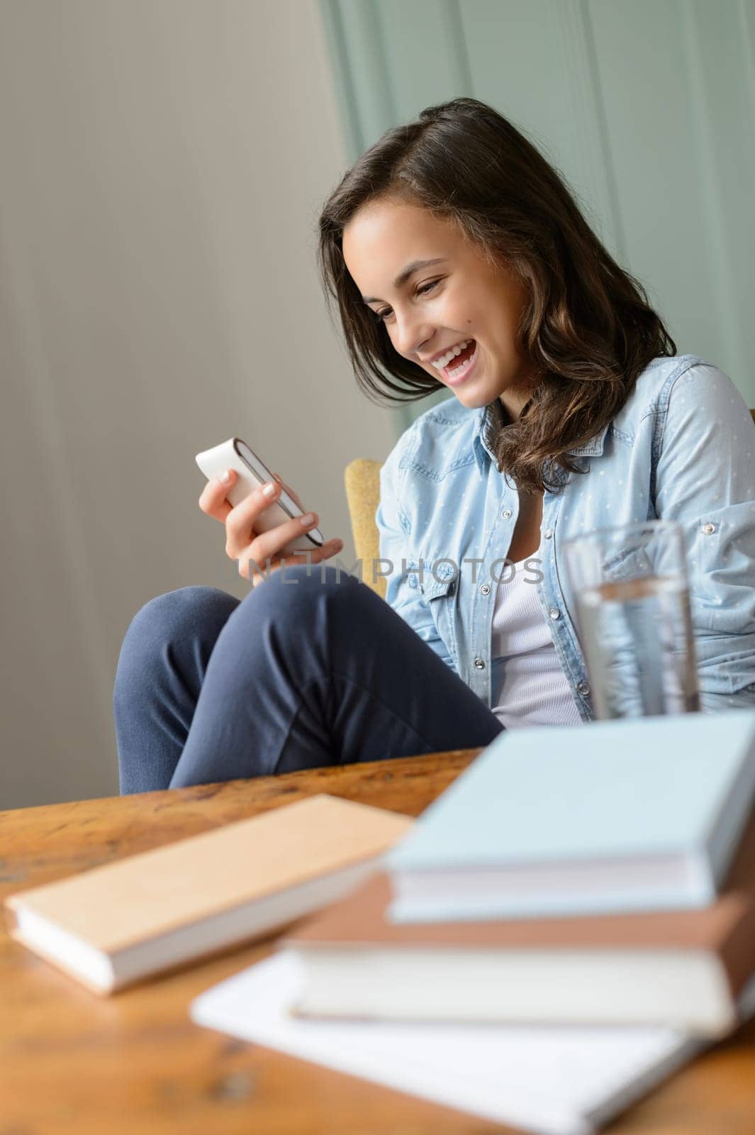 Cheerful teenage girl looking at mobile phone home read funny SMS