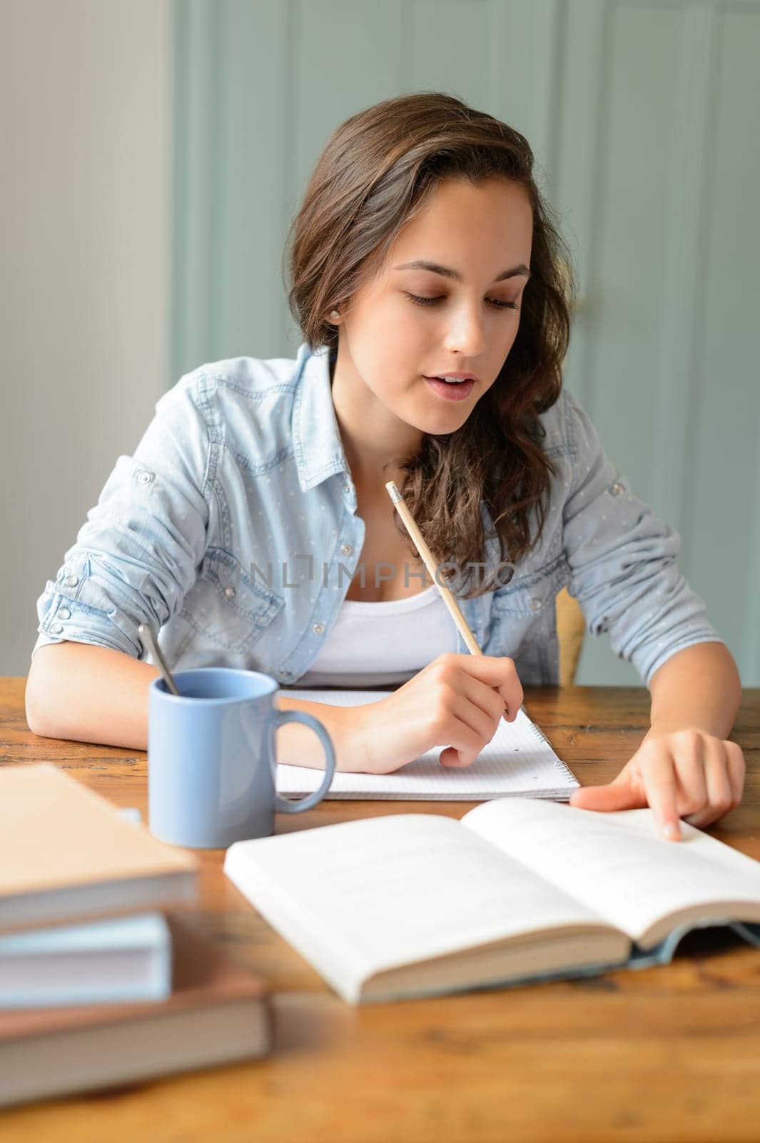 Teenage student girl studying book at home sitting behind table