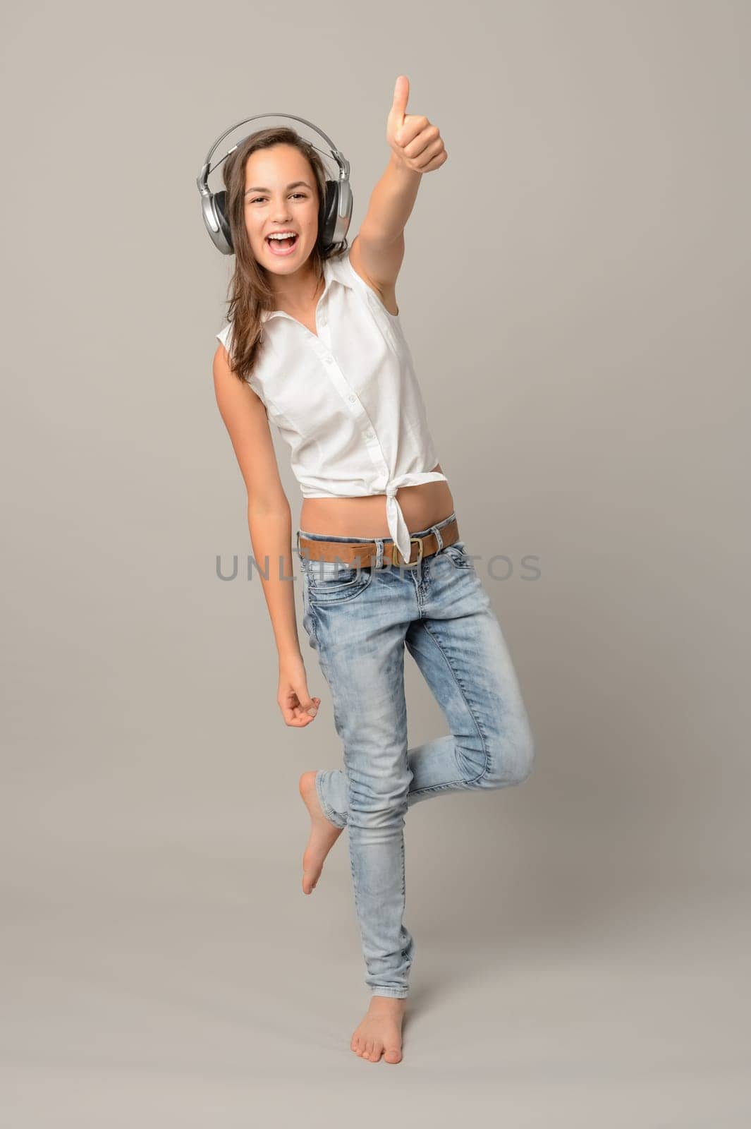 Girl enjoy listening music and dance thumb-up full length on gray