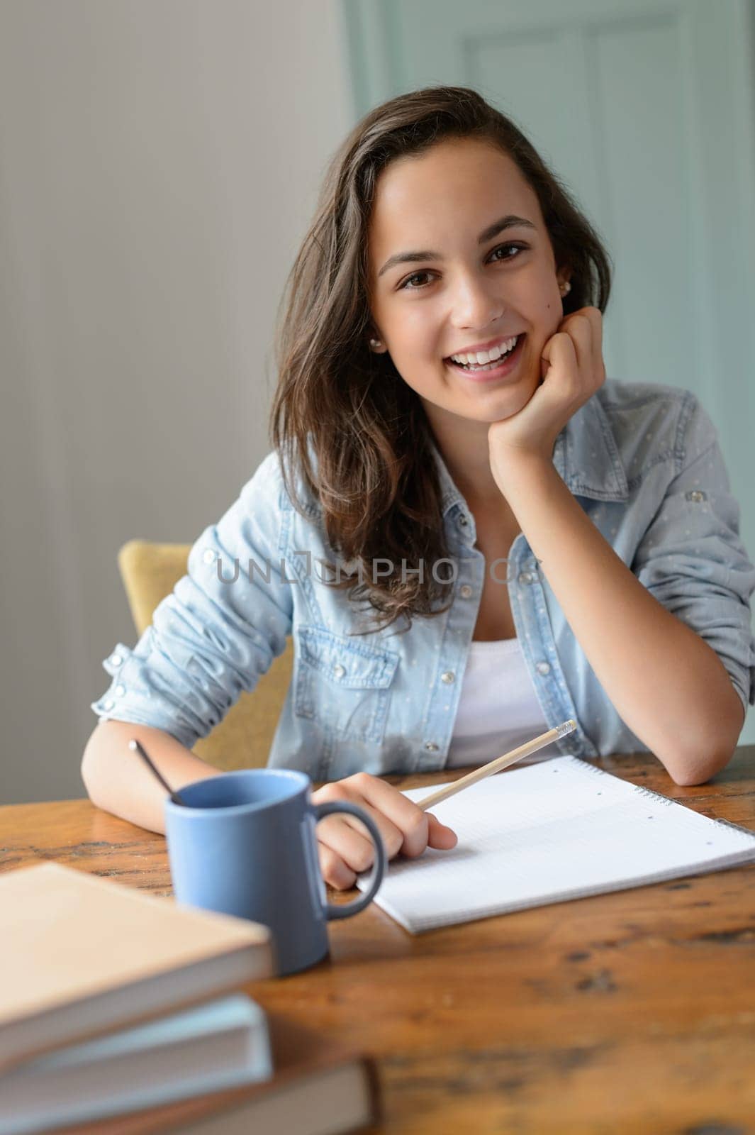 Teenage student girl studying at home smiling leaning against table