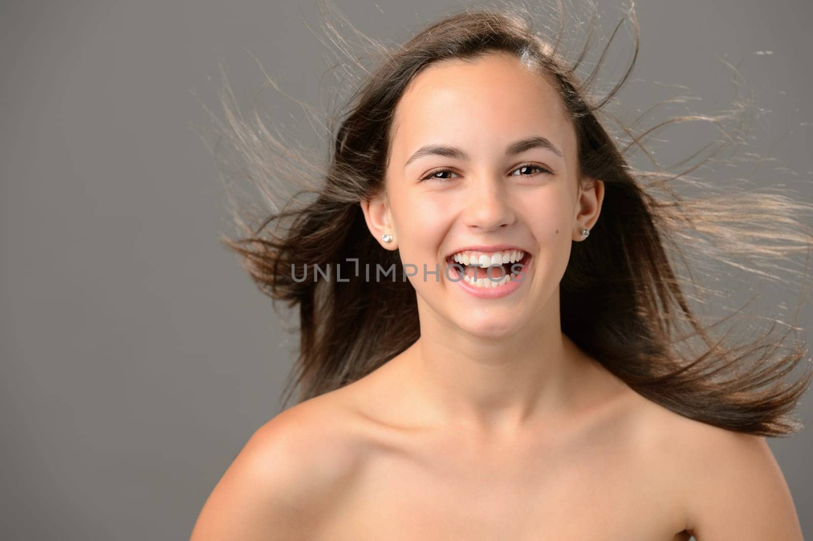 Laughing teenage girl blowing hair beauty skin on gray background