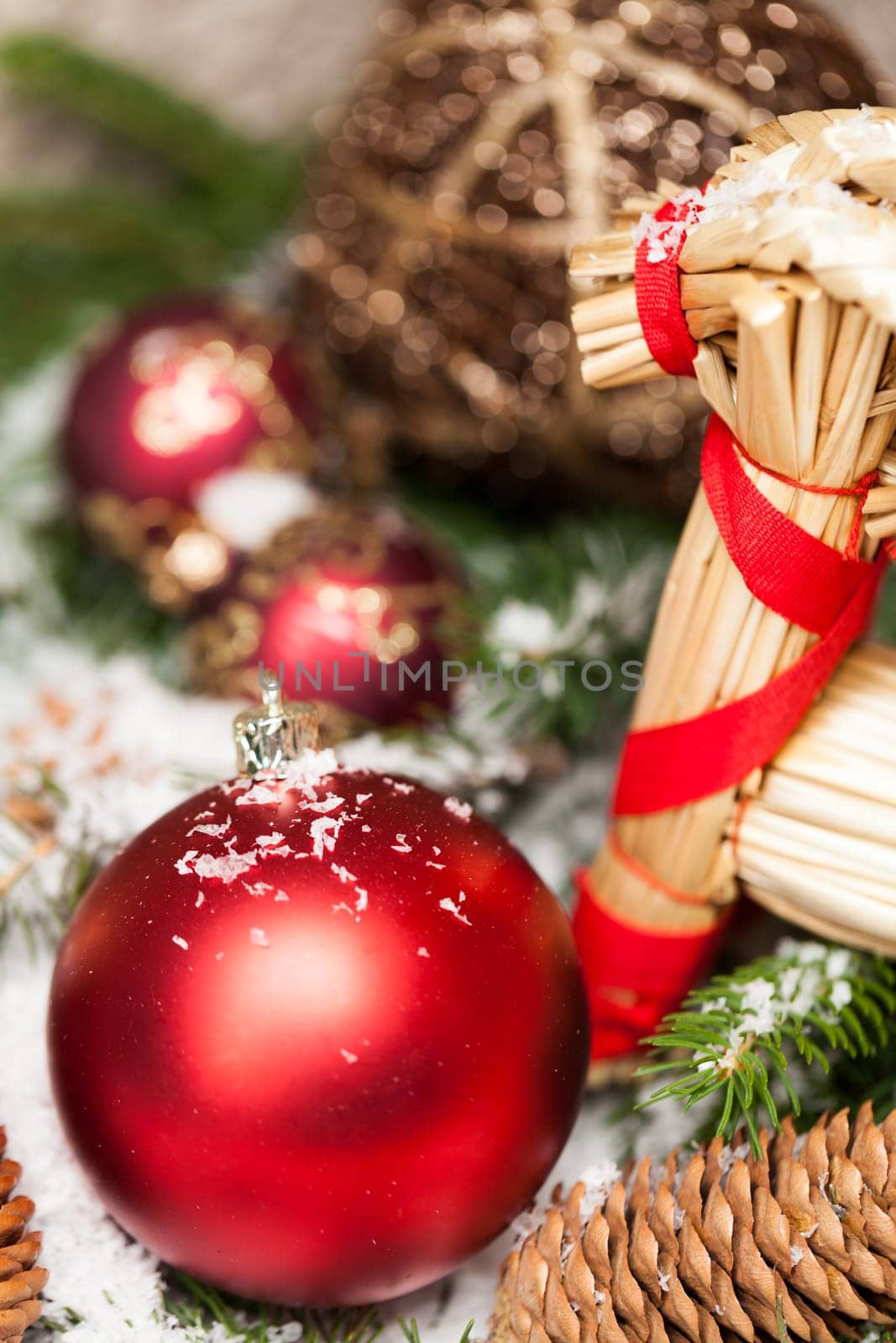 red Christmas baubles between cones and fir branches covered with snow as macro detail