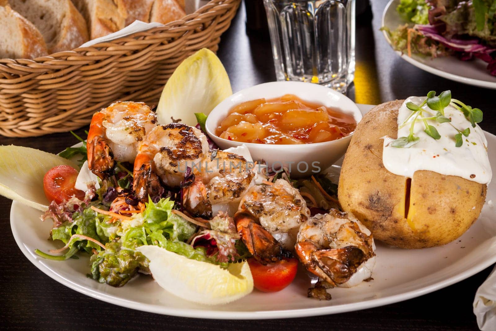 Roasted shrimp on a skewer on a mixed salad with dipp and foil potato on a plate