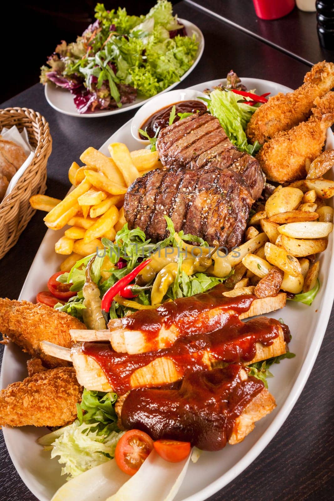 Huge barbecue plate with mixed meat and steaks on salad