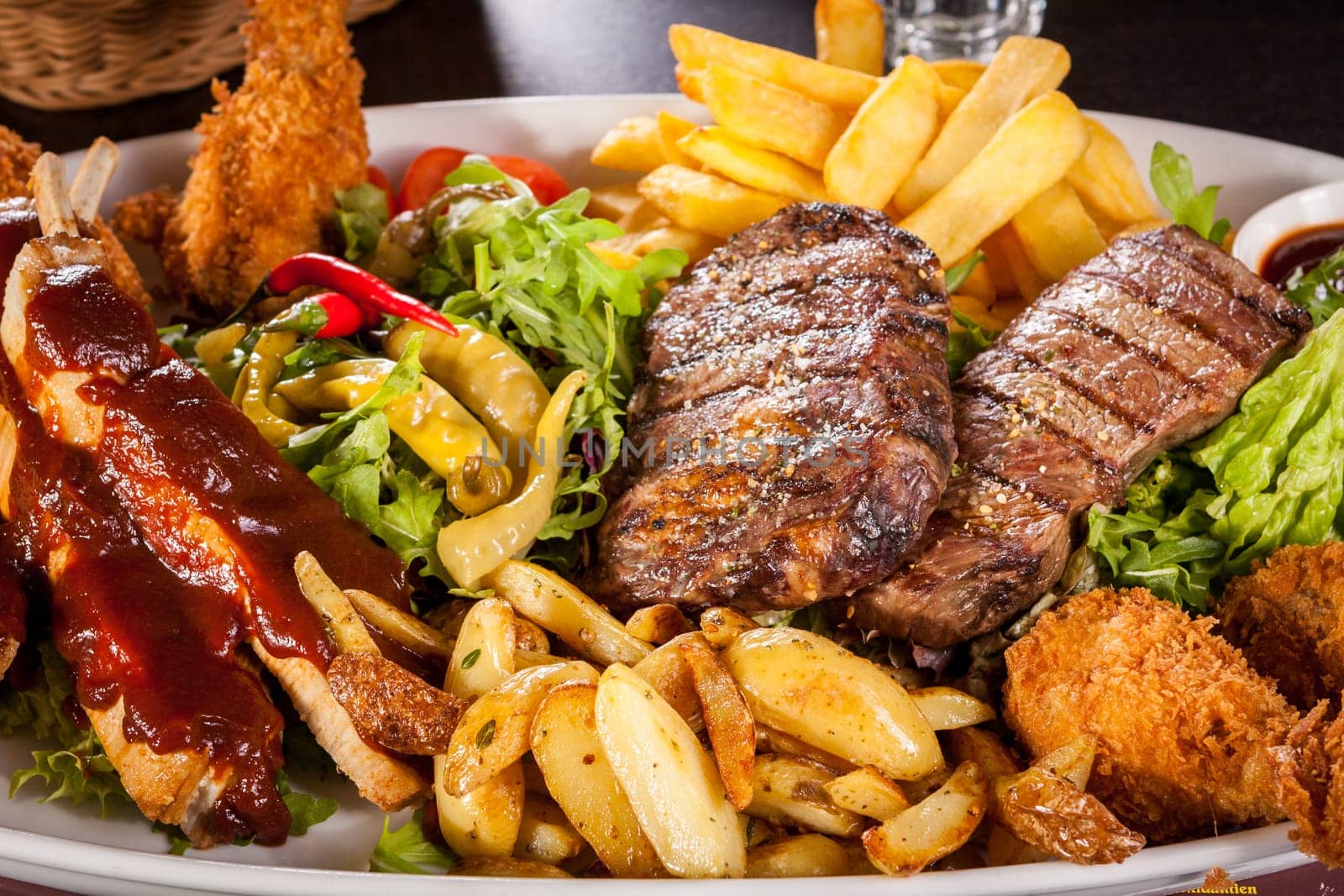 Huge barbecue plate with mixed meat and steaks on salad