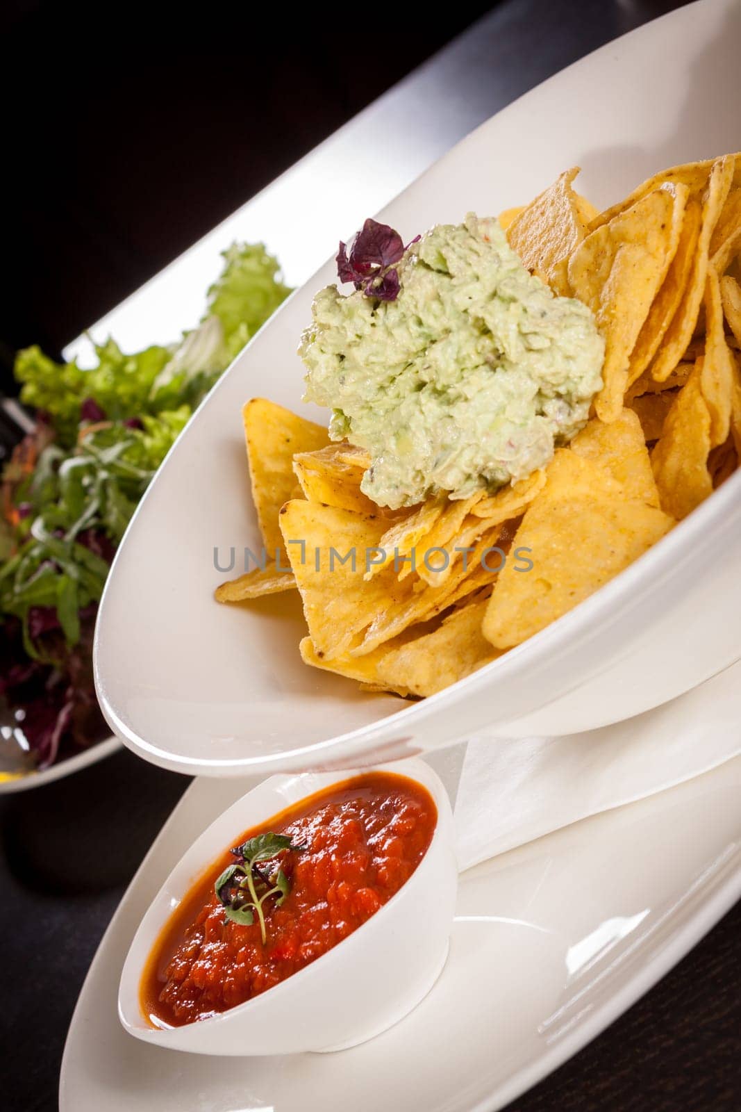 Corn chips nachos with guacamole and salsa dipp in a bowl on a plate