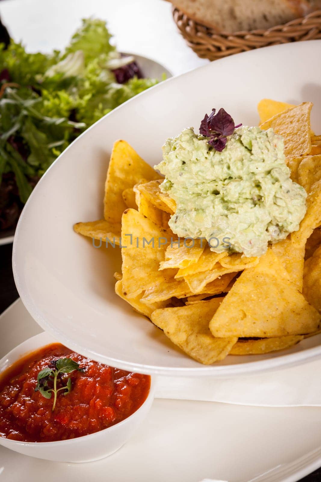 Corn chips nachos with guacamole and salsa dipp in a bowl on a plate