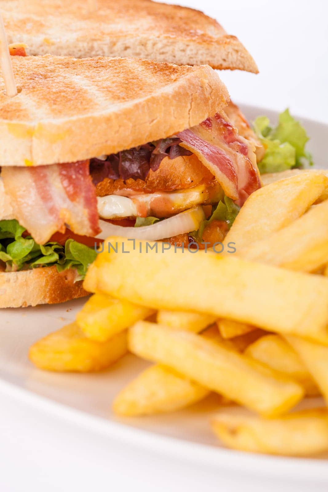 Club sandwich on toasted white bread with bacon and fries fried fries on a plate isolated against a white background