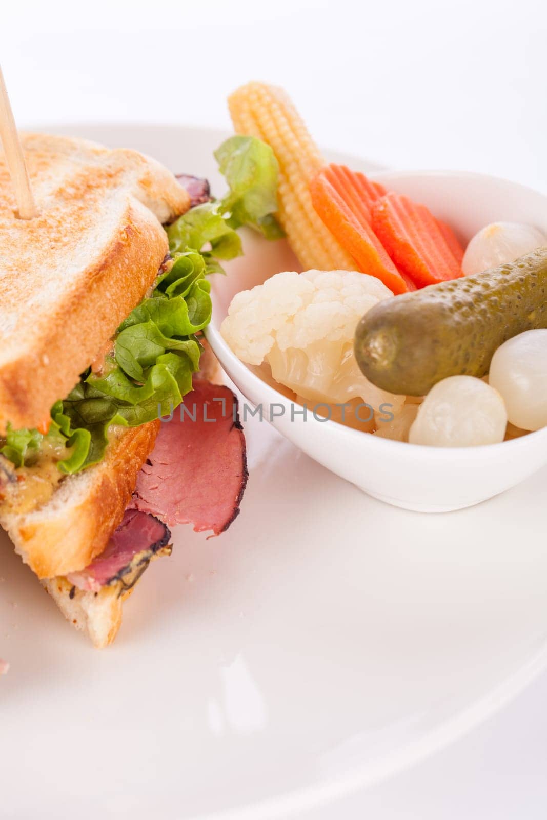 Delicious sandwich clubsandwich with bacon ham cheese and one with mixed pickels on a plate isolated against a white background