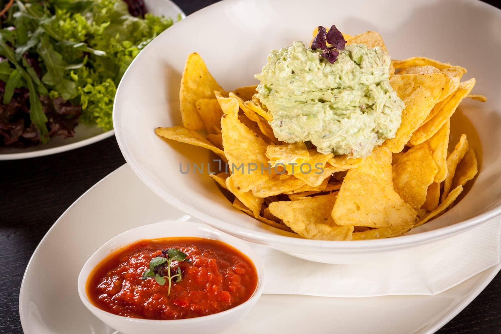 Corn chips nachos with guacamole and salsa dipp in a bowl on a plate