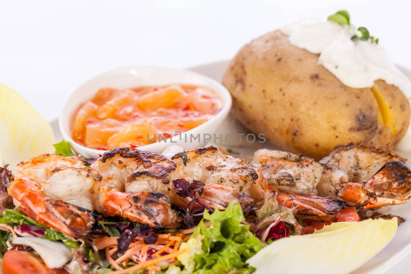 Roasted shrimp on a skewer on mixed salad with dip and foil potato prepared on a plate insulated against a white background