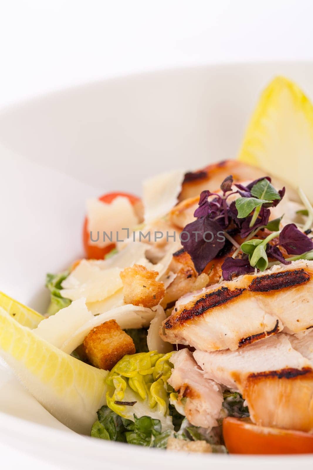 Fresh delicious caesarsalat with grilled chicken bust parmesan shards and croutons isolated against a white background