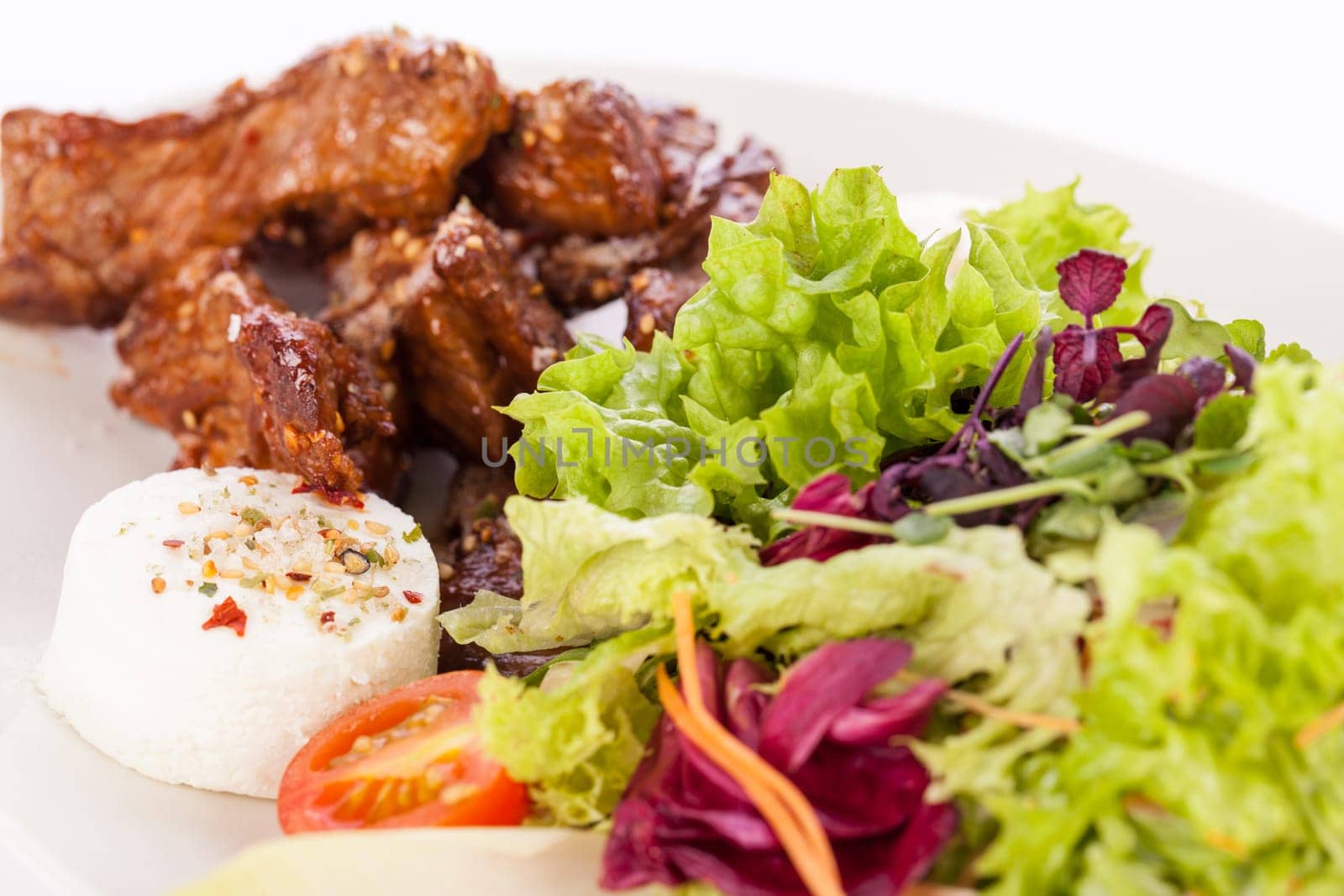 Fresh salad with fresh goat cheese and fried beef strips prepared on a plate insulated against a white background