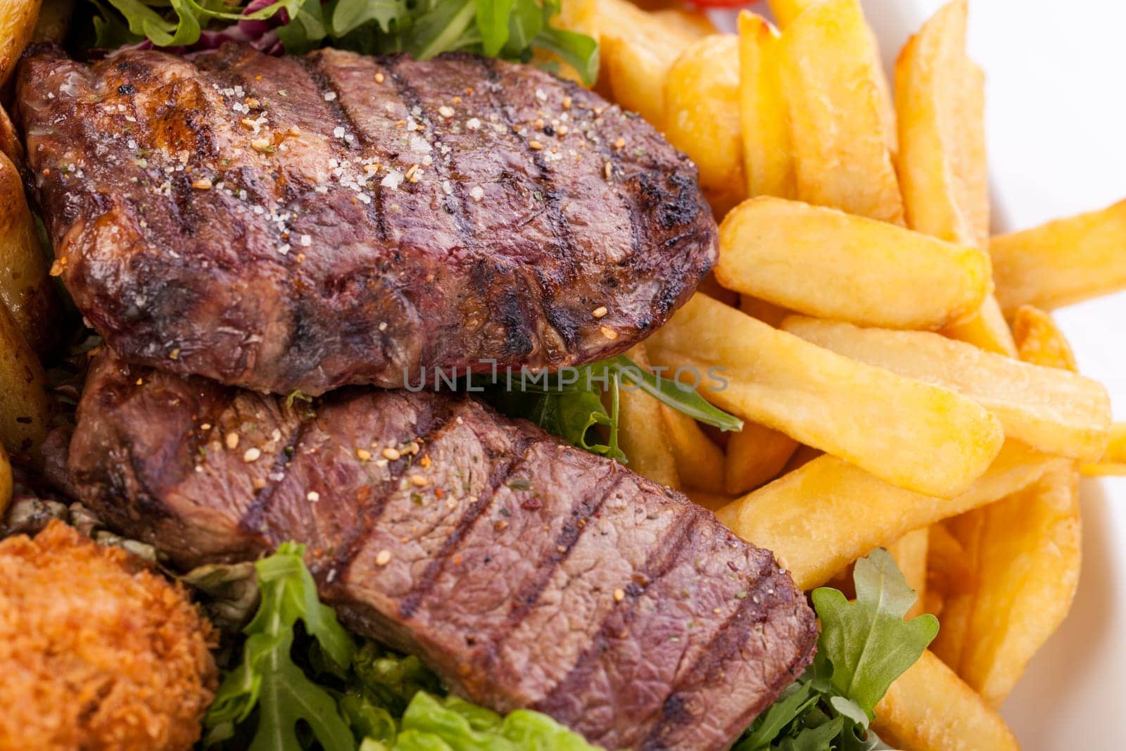 Huge barbecue plate with mixed meat and steaks on salad isolated against a white background
