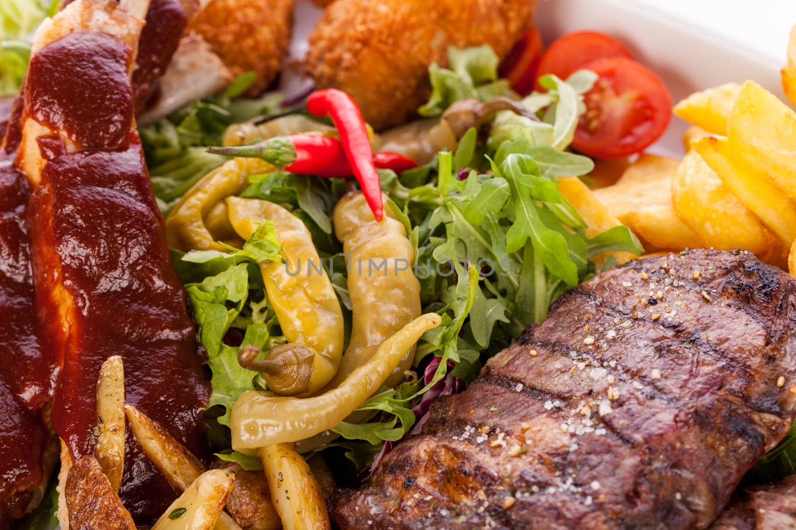 Huge barbecue plate with mixed meat and steaks on salad isolated against a white background