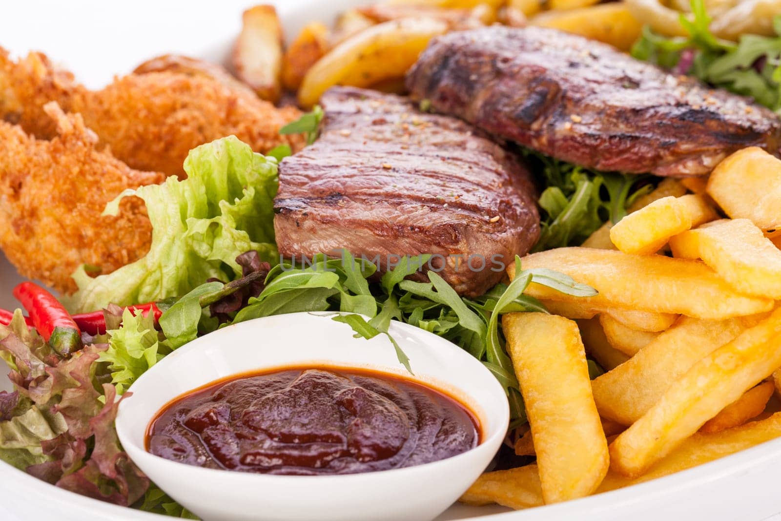 Huge barbecue plate with mixed meat and steaks on salad isolated against a white background