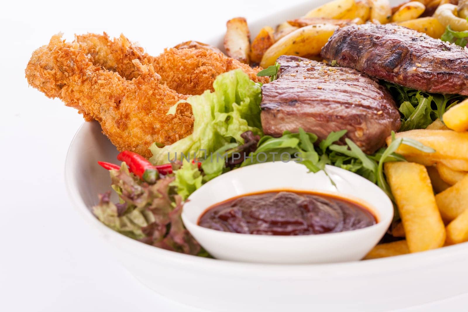 Huge barbecue plate with mixed meat and steaks on salad isolated against a white background